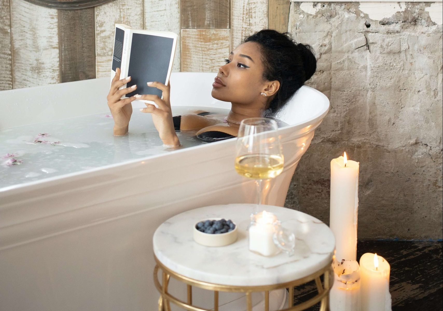 Young African lady relaxing in a bathtab as she reads a book